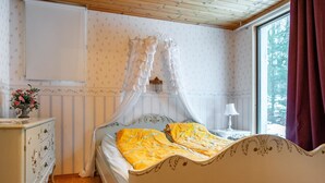 A bedroom with a canopy bed, a dresser, a nightstand, and a window with curtains.