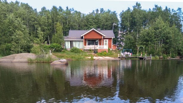 A house by a lake with a dock and chairs.