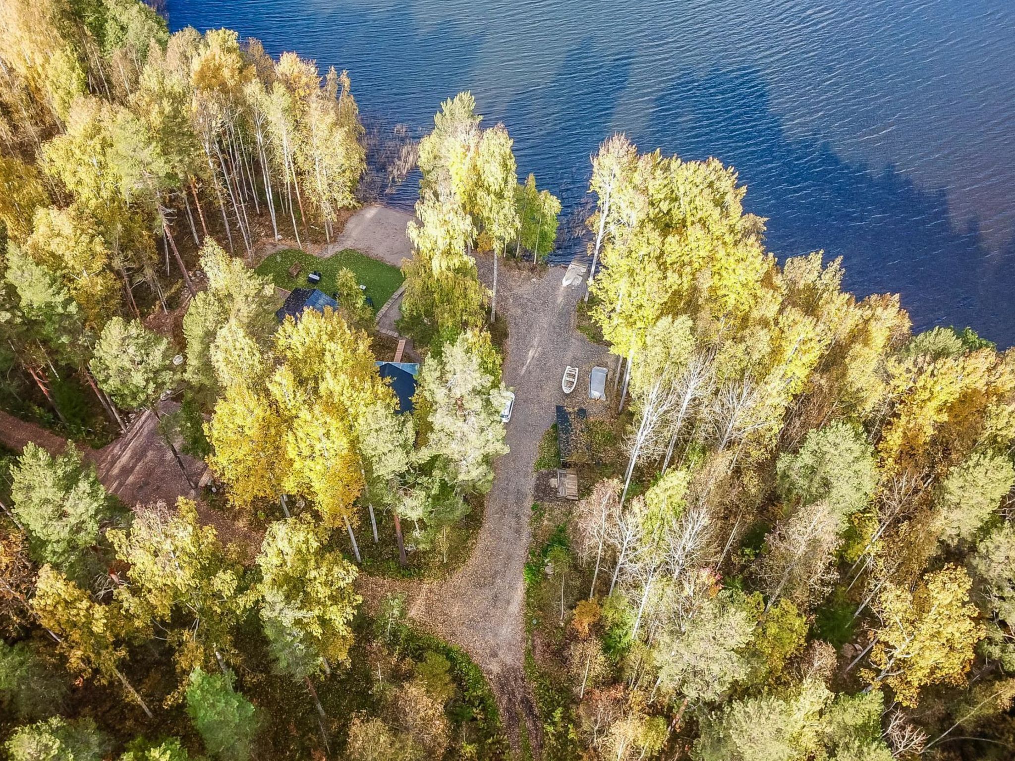 An aerial view of a lakeside property with a dock, a small boat, and a cabin surrounded by dense trees.