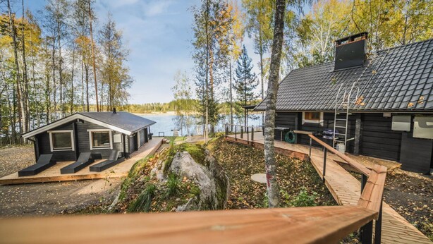 Une cabane dotée d’une terrasse donnant sur un lac, entourée d’arbres.