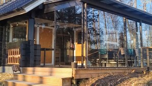 Une cabane avec une façade en verre, une terrasse en bois et une vue sur la forêt.