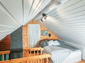 Une chambre à coucher aménagée en mezzanine, avec un plafond en pente, un lit, un banc en bois, une horloge et un tableau encadré au mur.