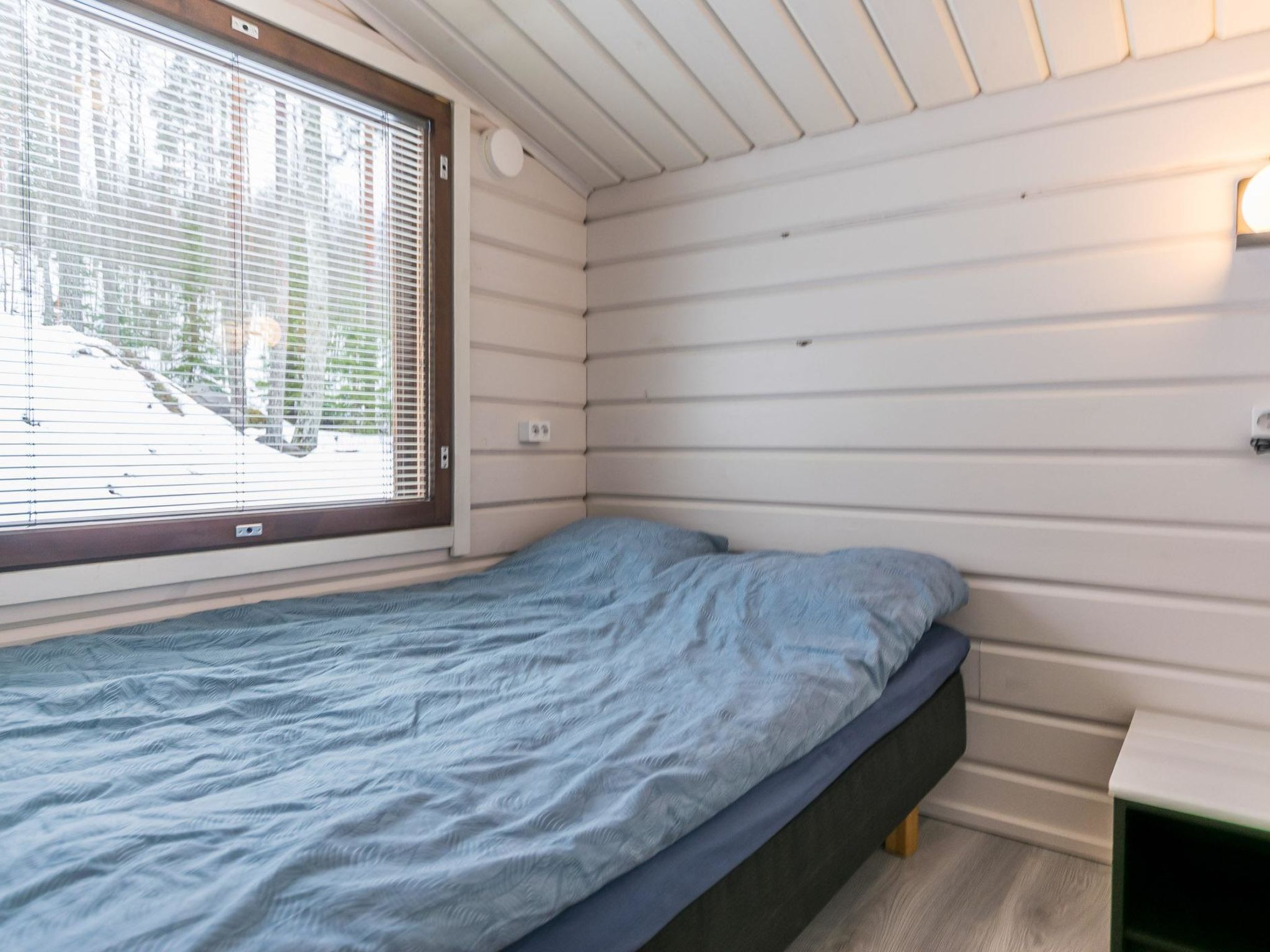 Ein kleines Zimmer mit einem Einzelbett, einem Fenster, weißen Wänden und einem Nachttisch in Grün.