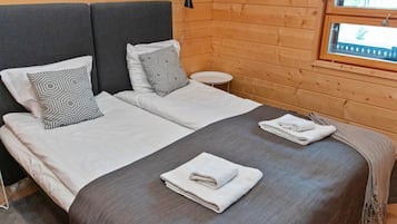 Ein Doppelbett mit grauer Bettwäsche und zwei Kissen, ein kleiner runder Tisch und ein Fenster mit Blick auf Gebäude.