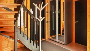 Un interior moderno con una escalera de madera, un perchero y una puerta con panel de vidrio.