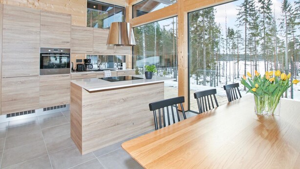 Una cocina moderna con armarios de madera, una isla central y un ventanal con vistas a un bosque nevado.