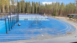 An outdoor sports court with a blue surface, surrounded by a fence, and a bench.