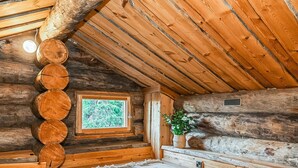 A log cabin interior with a sloped ceiling, a window with a view of greenery, and a woven basket with plants. - Rukan pilvimaja by Interhome (Kuusamo)