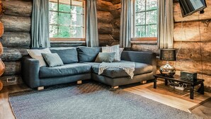 A log cabin interior with a sectional sofa, two windows with curtains, a lamp, and a small table with a radio. - Rukan pilvimaja by Interhome (Kuusamo)