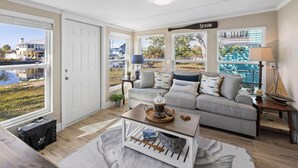A living room with a grey sofa, a coffee table, and a view of a pool and houses. - Boat, Kayak & Relax: Stunning Waterfront Home w/ Sunsets and Direct Gulf Access (Hernando Beach)