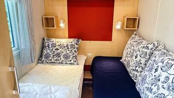 A small, compact room with two beds, a red accent wall, and two bedside tables with lamps.