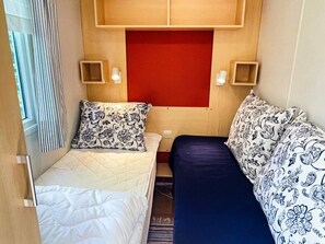 A small, compact room with two beds, a red accent wall, and two bedside tables with lamps. - 4 Person Holiday Home in Hollviken (Hollviken)