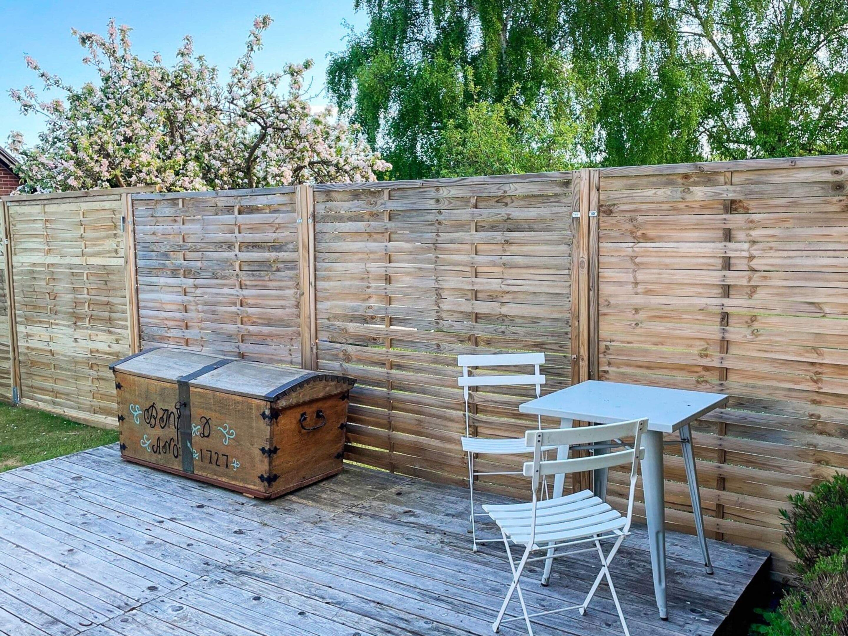 Um deck de madeira com mesa, cadeiras, um baú e cerca de madeira.