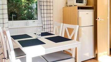 A compact kitchen with a white table, two chairs, a microwave, and a refrigerator.