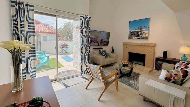 A living room with a sofa, a coffee table, a TV, a fireplace, and a view of the outside. - Downtown Palm Springs Holiday Loft, View Patio (Palm Springs)