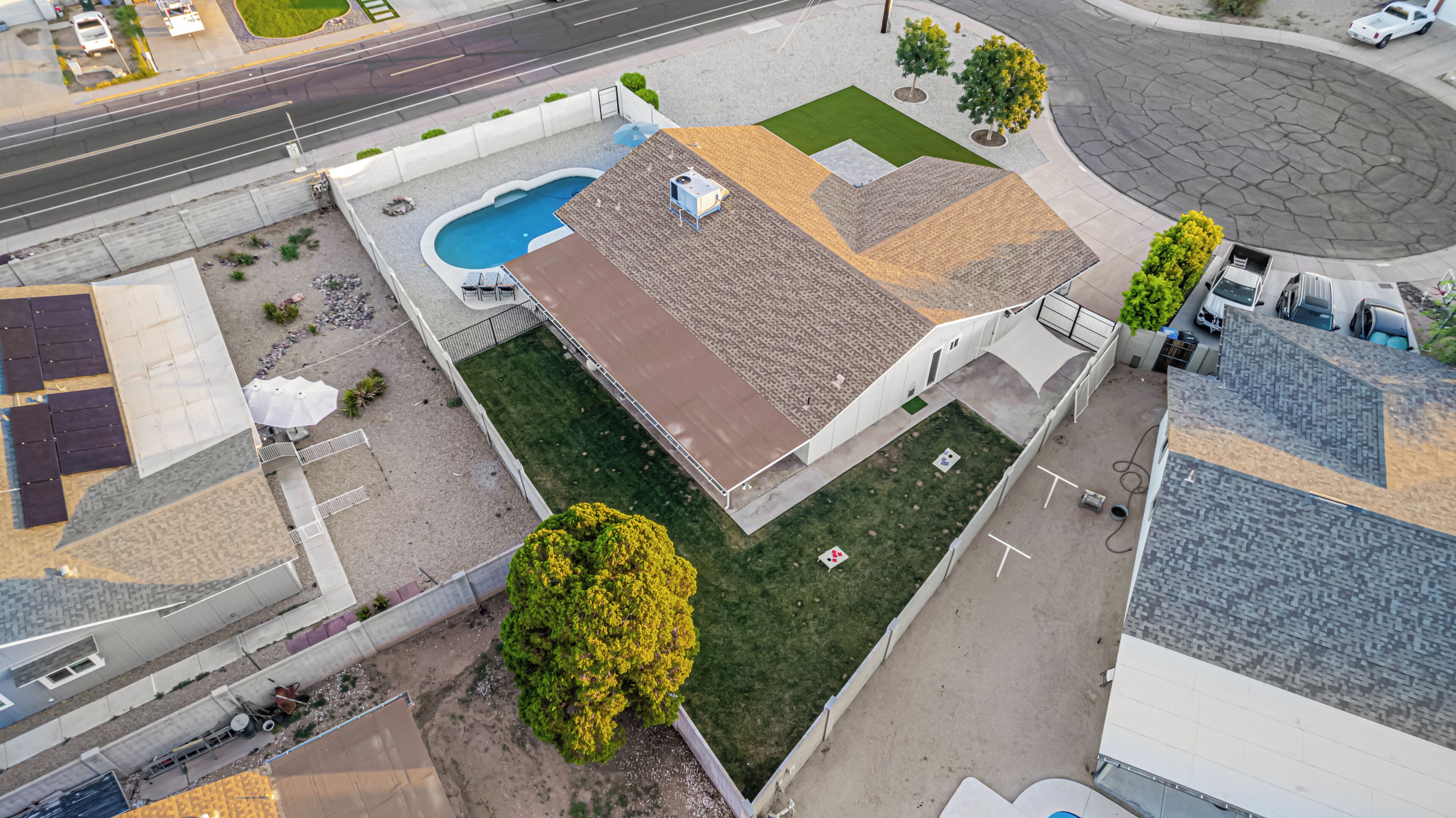 An aerial view of a property with a swimming pool, a covered patio, and a fenced yard.
