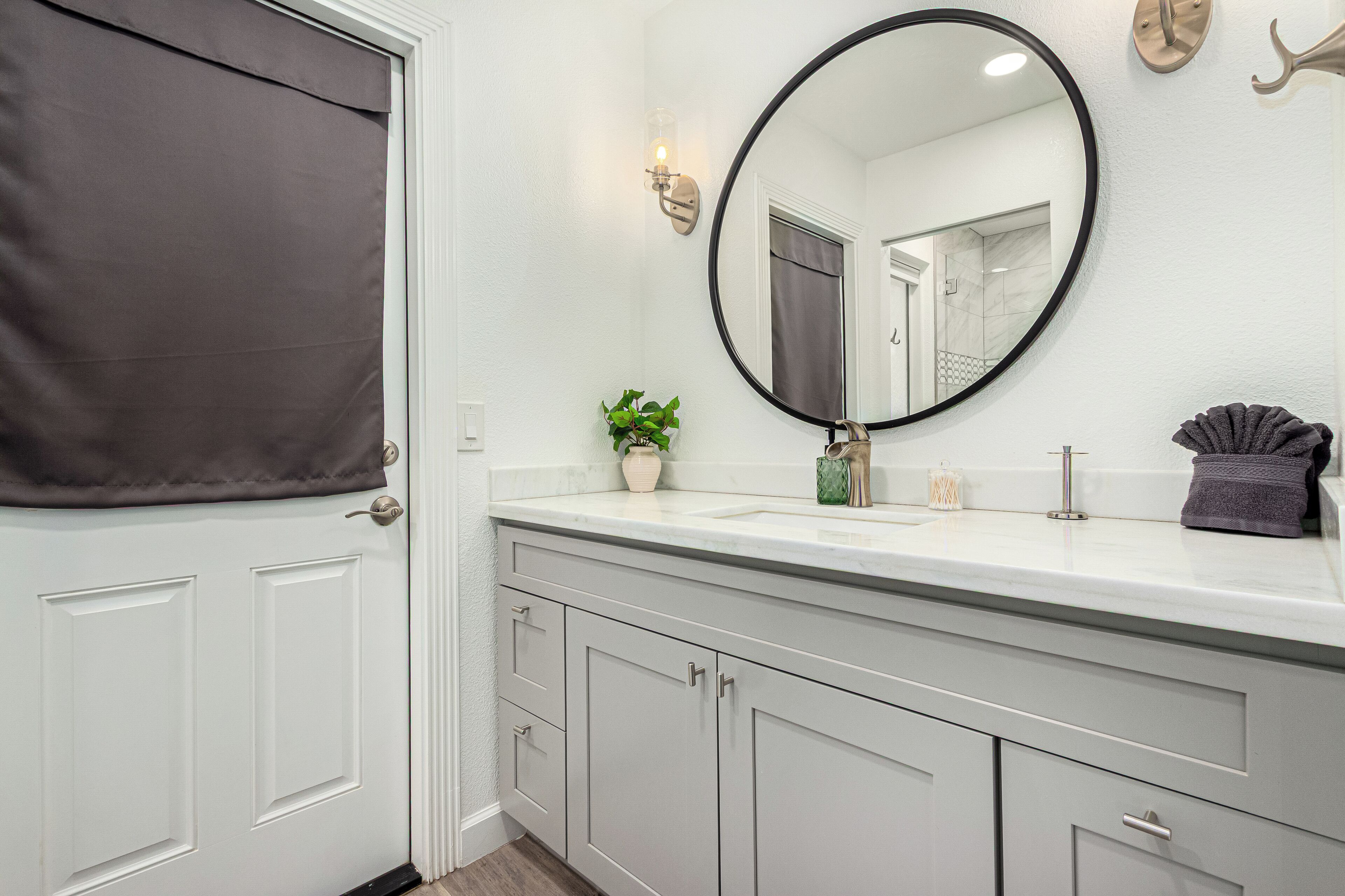 A bathroom with a white vanity, a round mirror, a potted plant, and a towel rack.