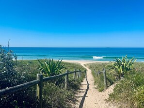 A sandy beach path leading to the ocean with a clear blue sky.