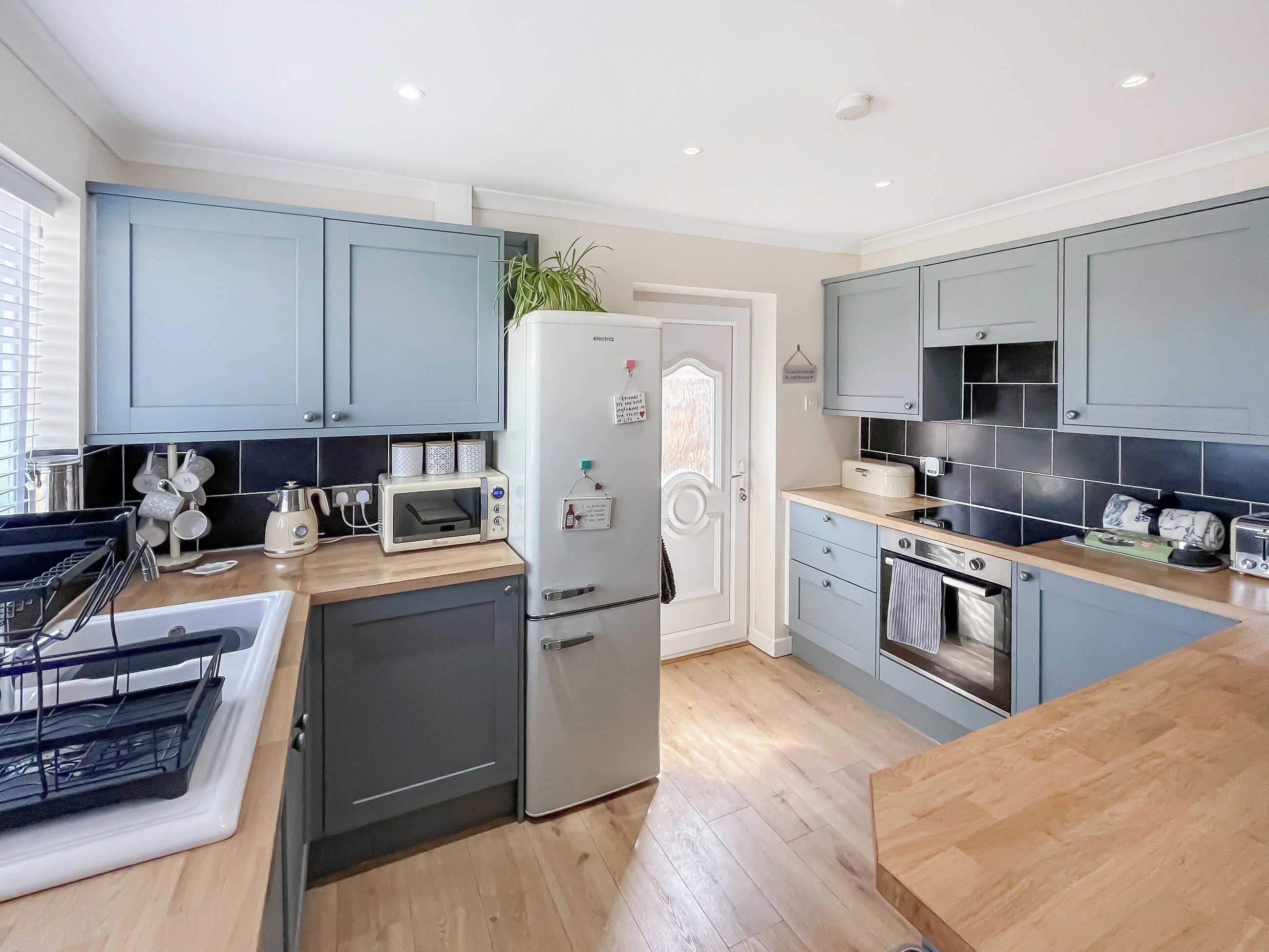 A modern kitchen with grey cabinets, a built-in microwave, a refrigerator, and a wooden countertop.