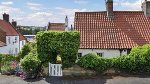 A traditional building with a red-tiled roof, a white gate, and lush greenery.