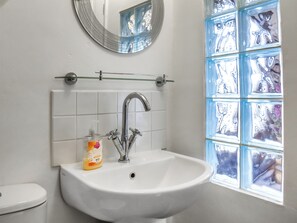 Een badkamer met een wit wastafelmeubel, een spiegel en een raam met blauwe ruiten.