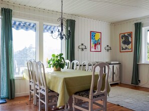 A dining area with a table, chairs, a chandelier, artwork, and a view through the window. - 5 Star Holiday Home in Stromstad (Stromstad)