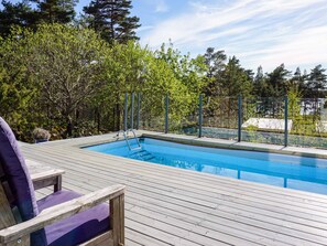A swimming pool with a wooden deck, surrounded by trees and a fence. - 5 Star Holiday Home in Stromstad (Stromstad)