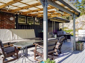 An outdoor patio with a wooden deck, a covered seating area with a sofa and chairs, a table, and a barbecue grill. - 5 Star Holiday Home in Stromstad (Stromstad)