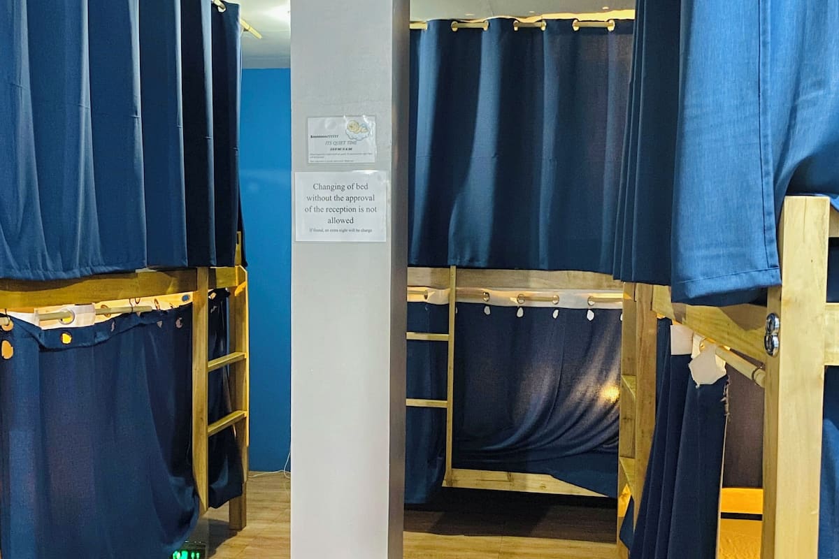 Habitación con literas, cada una con cortina. Un letrero indica que no está permitido cambiar la ropa de cama sin autorización.