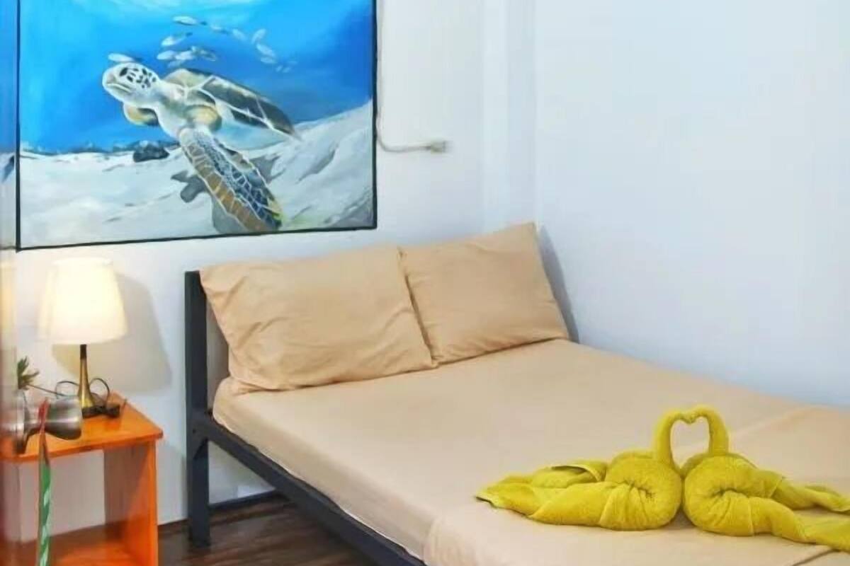 Un dormitorio con una cama, un cuadro de una tortuga marina, una lámpara de noche y un aire acondicionado instalado en la pared.