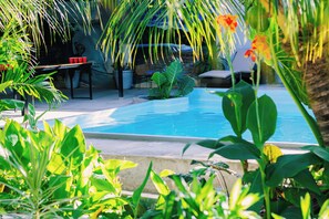 A pool surrounded by lush greenery and a dining area with chairs and a table. - Ananas Guesthouse (Moalboal)