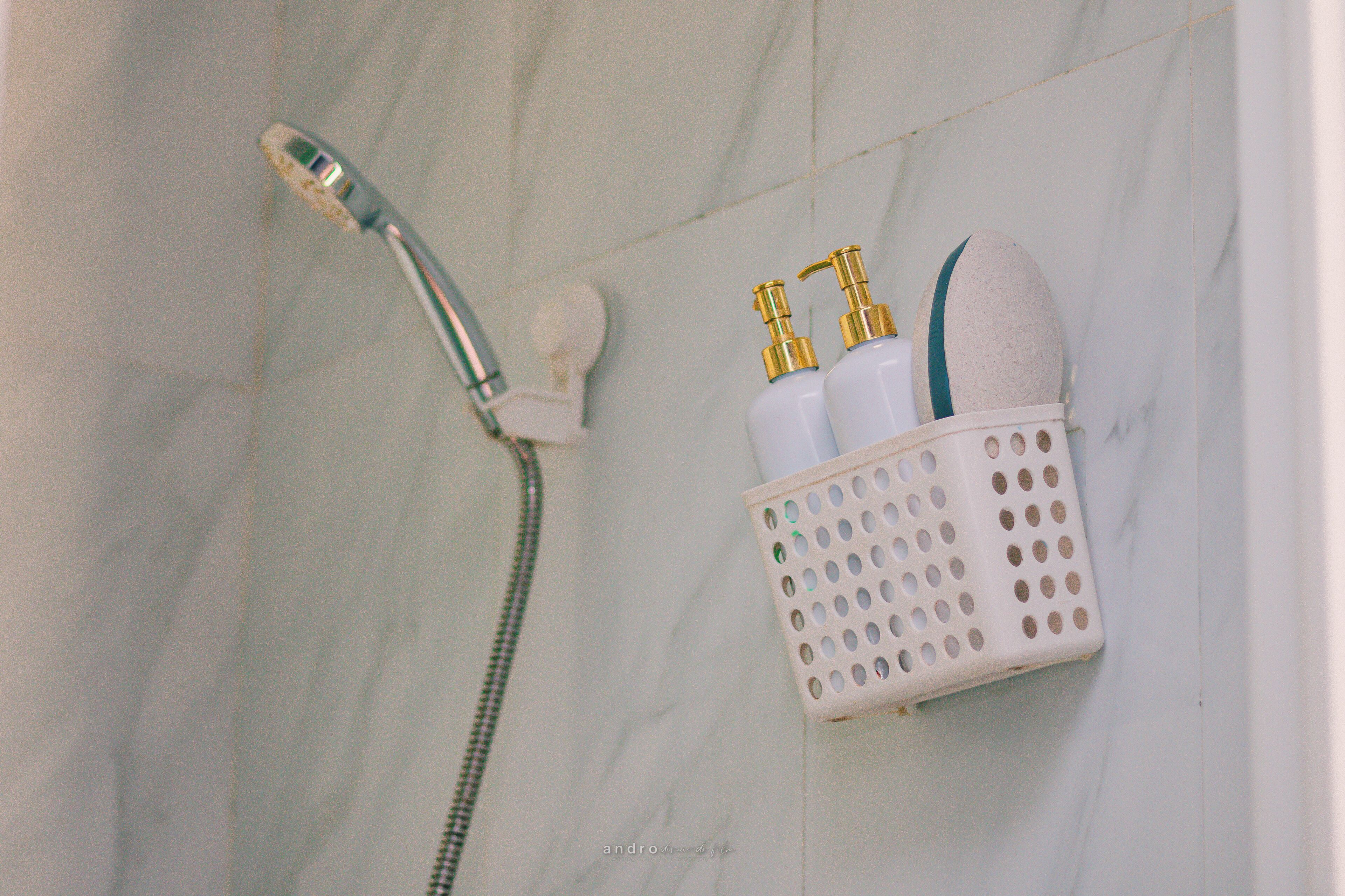 A bathroom with a shower, a white marble wall, and a basket containing toiletries.