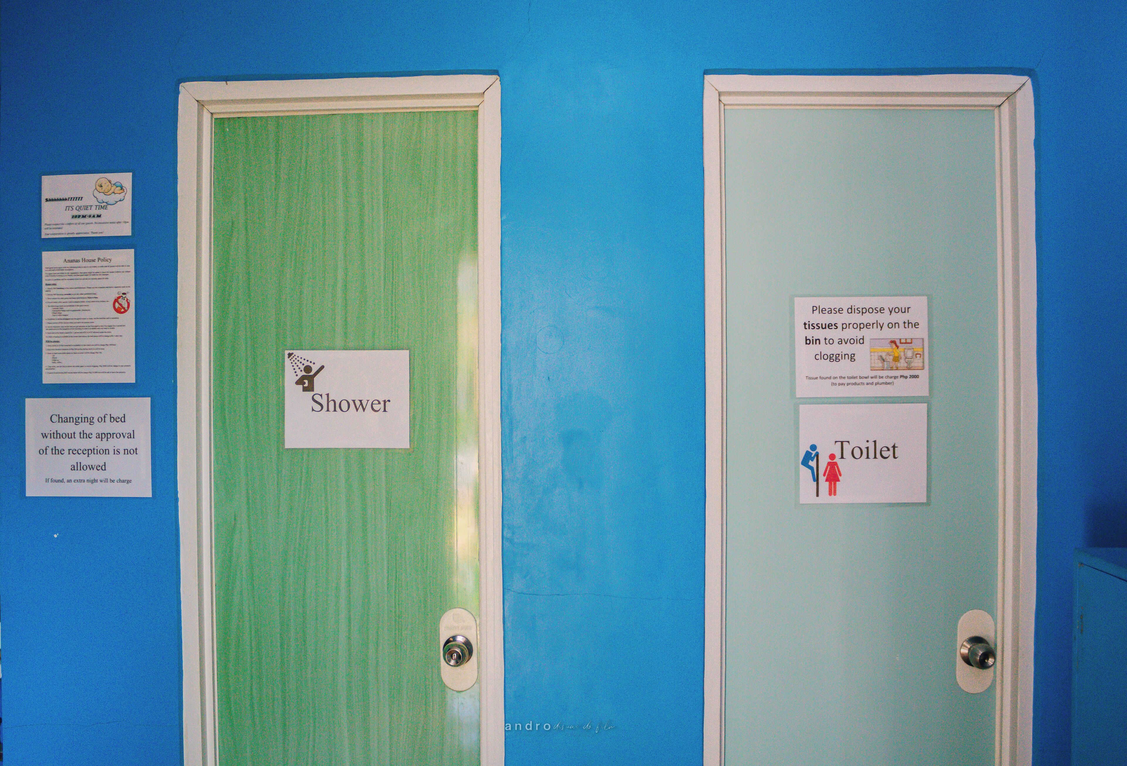 Deux portes, l’une portant l’inscription « Douche » et l’autre « Toilettes », avec des panneaux indiquant la manière appropriée d’éliminer les mouchoirs et un avis concernant la politique de changement des draps.