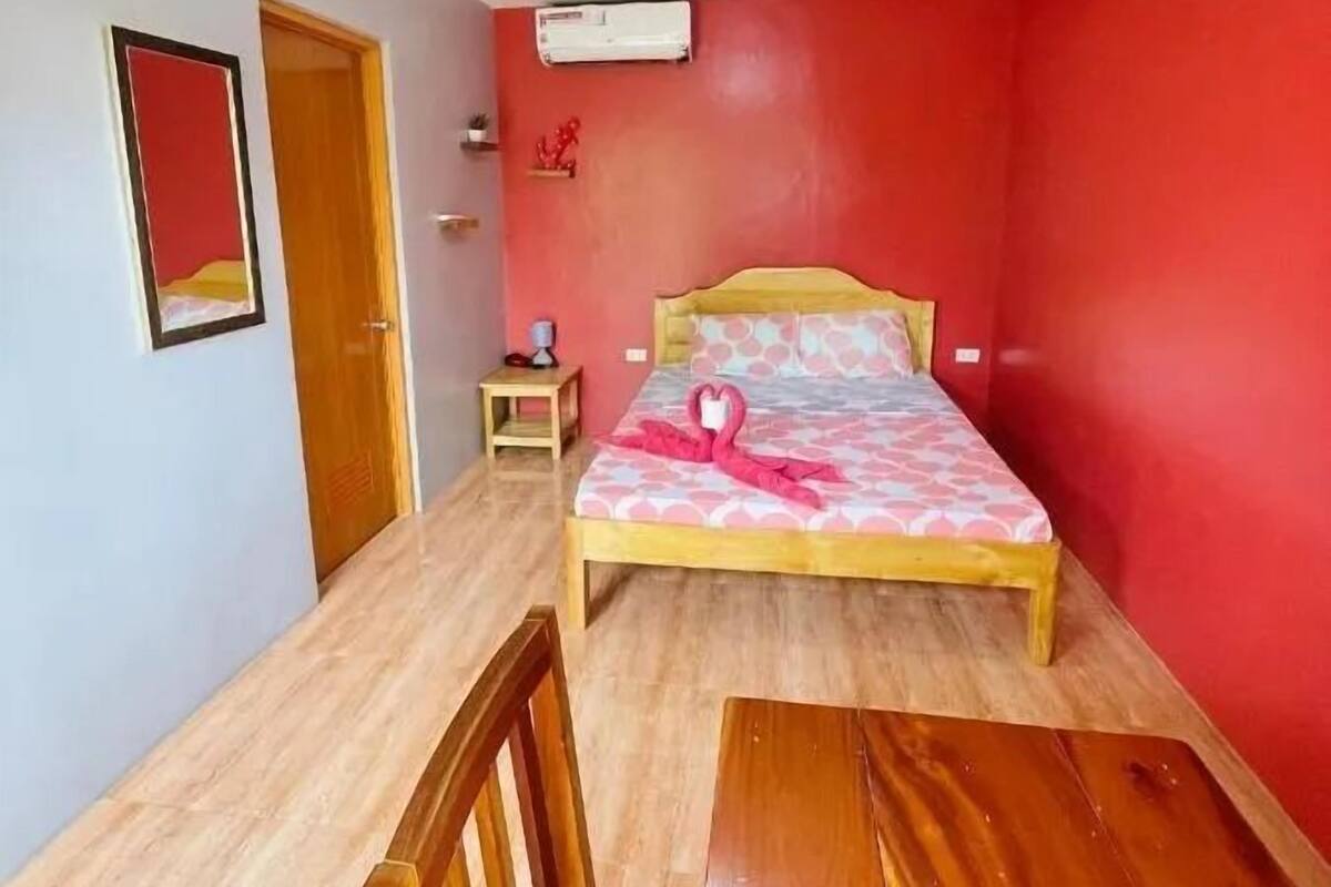 Un dormitorio con cama, mesita de noche, una silla, una mesa de madera, un espejo y un equipo de aire acondicionado.