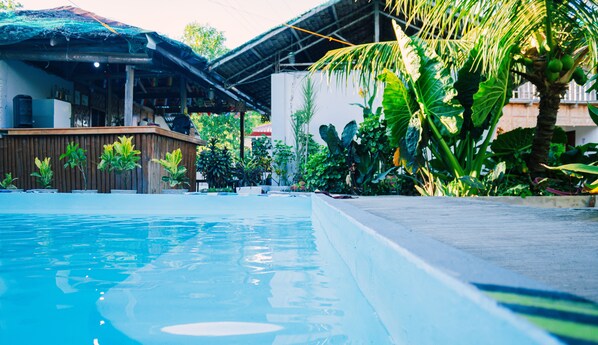 A swimming pool with a wooden deck and tropical plants. - Ananas Guesthouse (Moalboal)