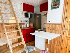 A compact kitchen with a wooden ladder, red cabinets, a white countertop, and a microwave. - 4 Person Holiday Home in Borgholm (Borgholm)