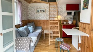 Un espacio habitable pequeño con cama tipo loft, kitchenette y un rincón de comedor.