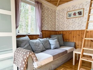 A cozy room with a wooden bench, a sofa with cushions, a window with curtains, and a wall with floral wallpaper. - 4 Person Holiday Home in Borgholm (Borgholm)