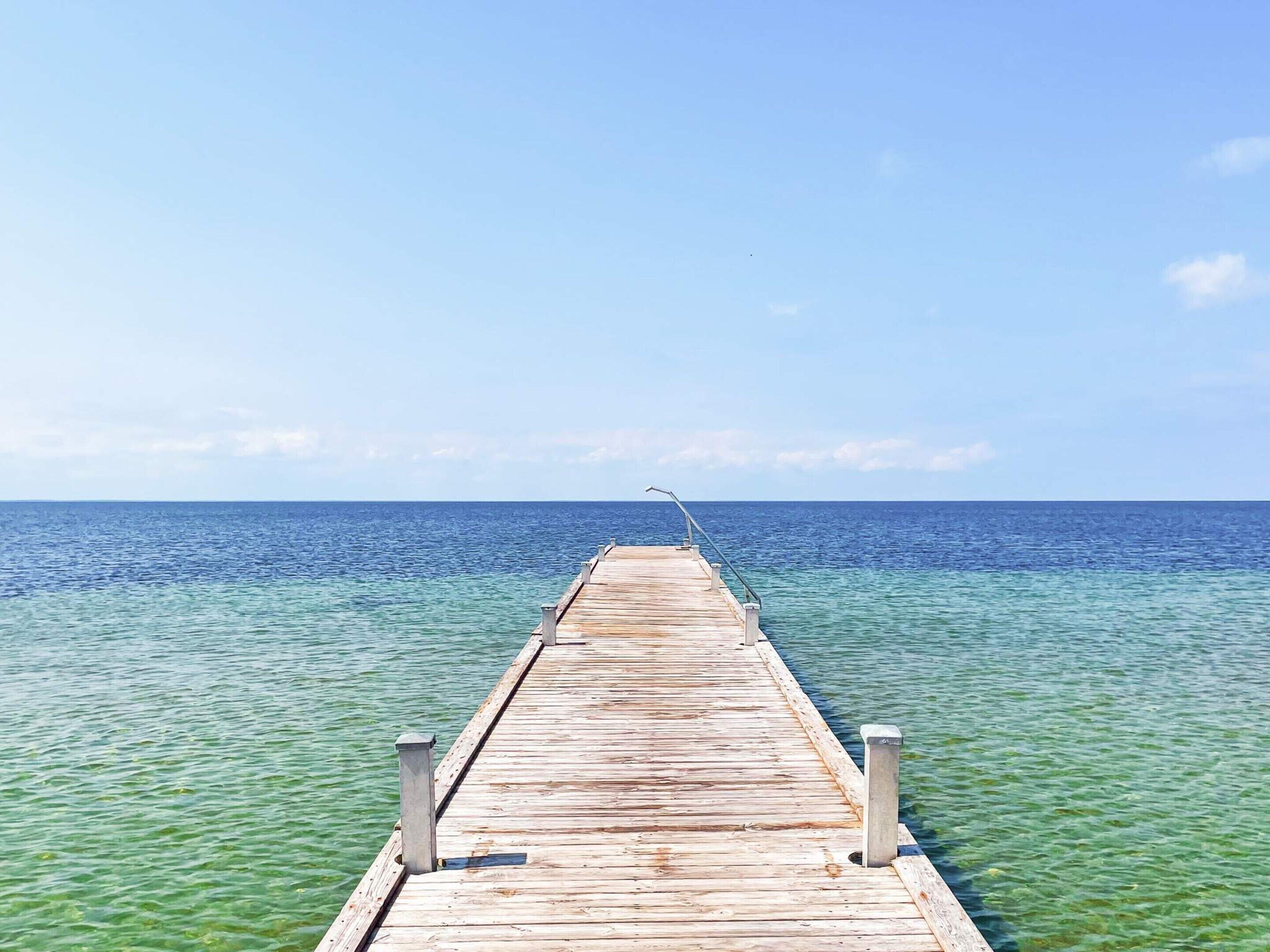 A wooden pier extending into a calm sea with clear water and a clear sky.