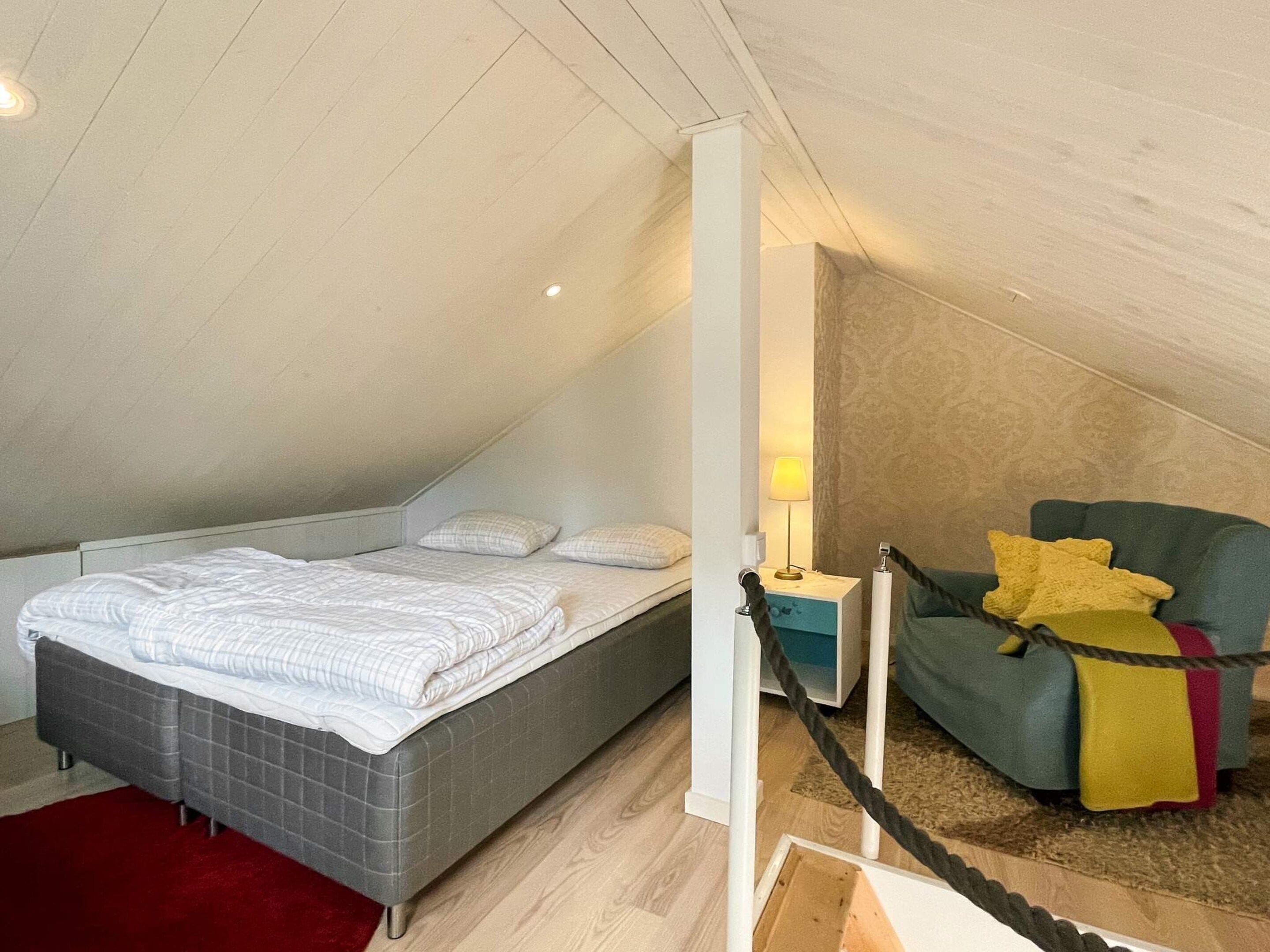 Un dormitorio con cama, mesita de noche, lámpara y una silla.