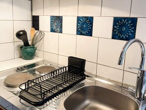 A kitchen with a stainless steel sink, a black dish rack, and a green pot with utensils.