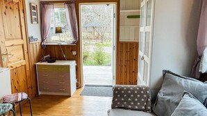 Una habitación acogedora con una puerta de madera, un pequeño escritorio con cajones, una ventana con cortinas, un sofá con cojines y vistas al exterior.