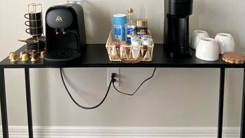 Una estación de café con una cafetera, un cesto de cápsulas de café, una máquina Nespresso y un molinillo.