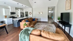 Un salón amplio con un sofá grande, un televisor y una cocina al fondo.