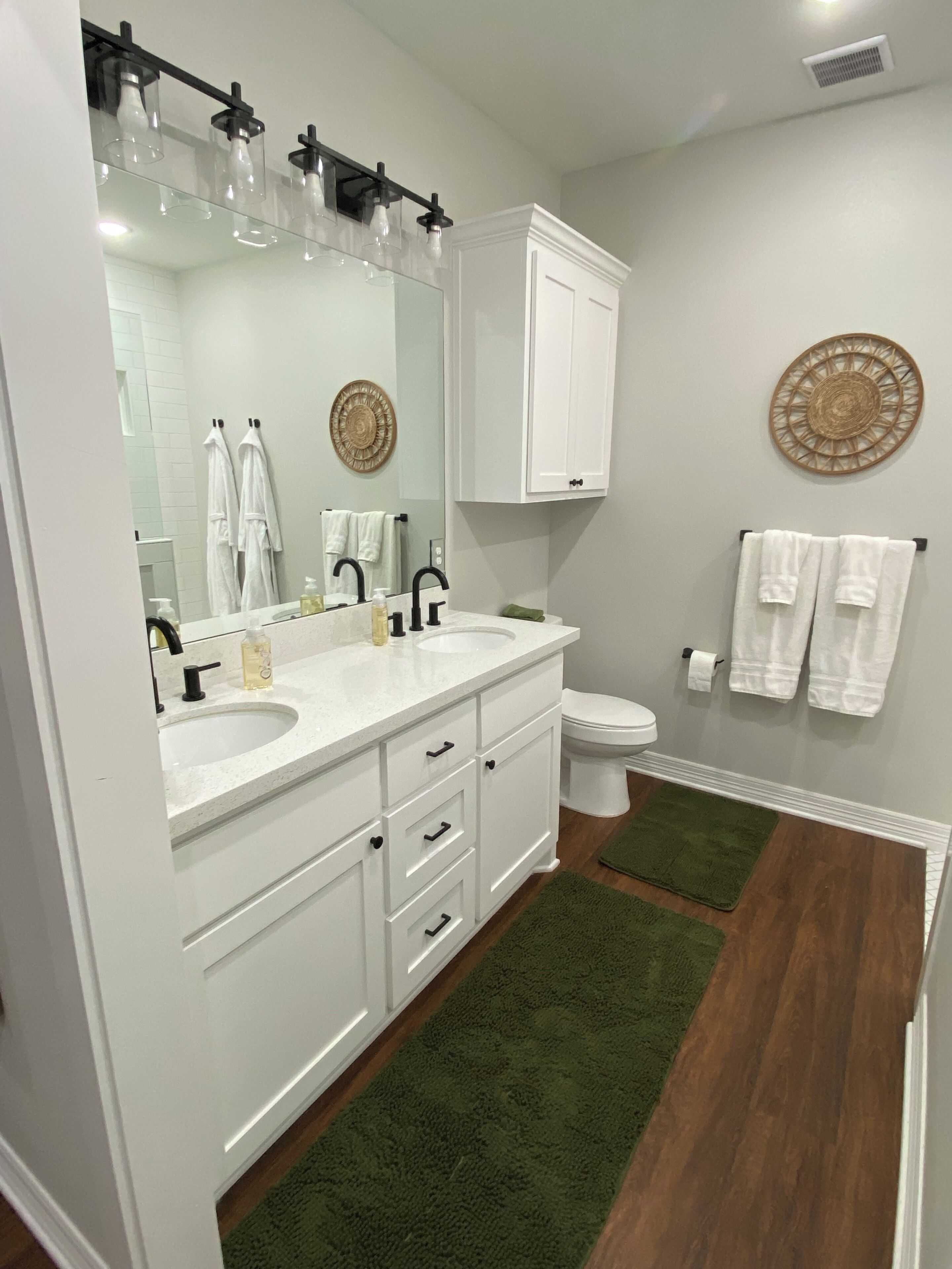 A bathroom with a white vanity, a large mirror, a toilet, and a green rug.