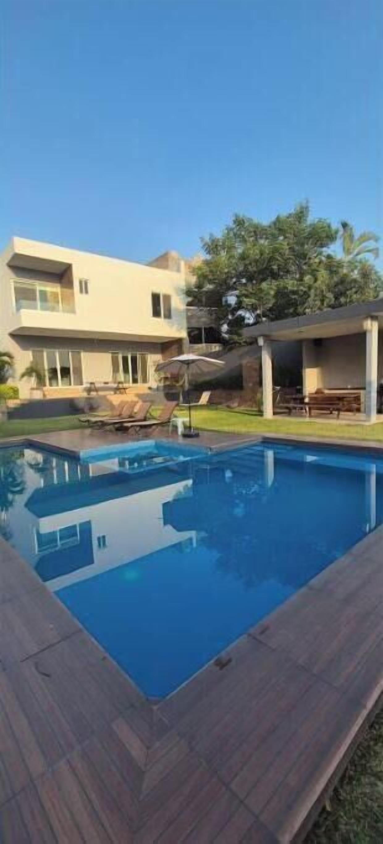 A modern house with a swimming pool, a covered patio, and a lawn.