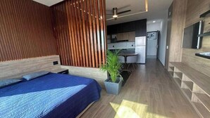 A modern bedroom with a large bed, a wooden slatted wall, a small kitchen area, and a potted plant. - Serenity Loft for relaxation with pool in Oaxtepec (Oaxtepec)