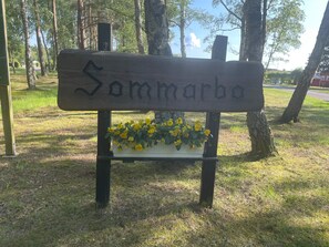 Een houten bank met de naam 'Sommarbo' in gegraveerd, omringd door gras en bomen.