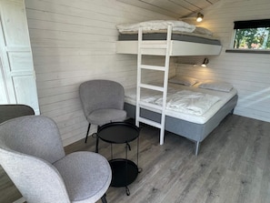 Een stapelbed met een ladder, een grijze stoel en een klein tafeltje in een kamer met houten wanden en een raam.