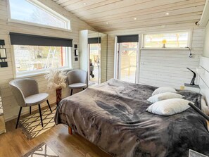 A bedroom with a bed, two chairs, a window, and a door leading outside.